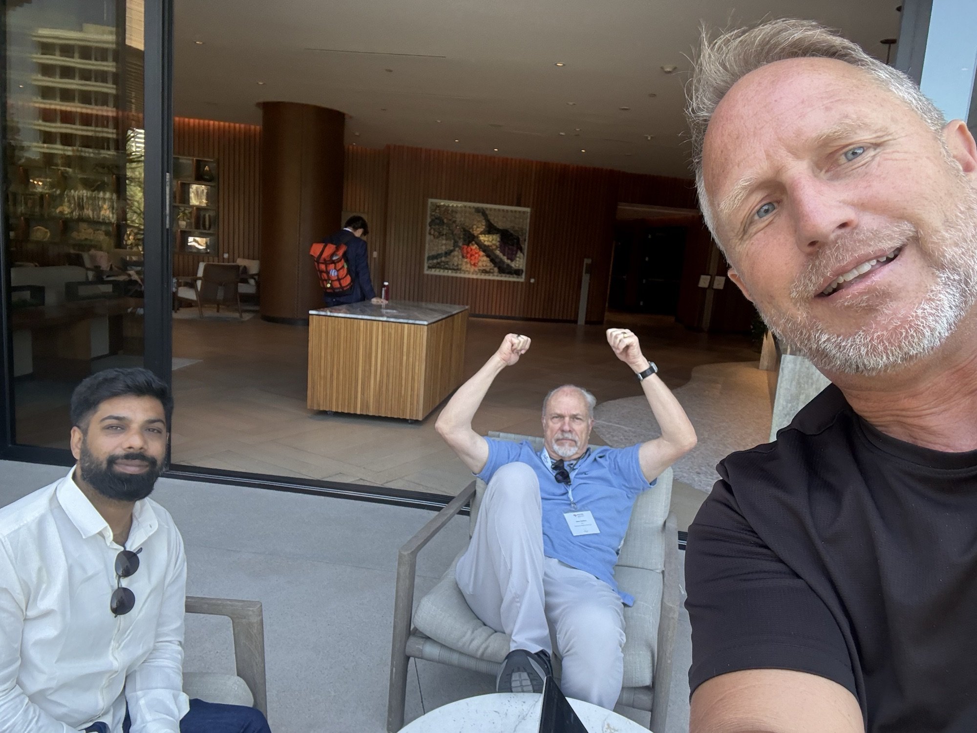 Three men gathered by a lounge seating area, with one taking a group selfie.